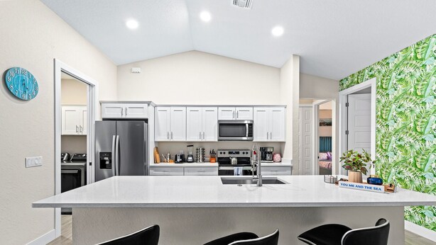 A modern kitchen with white cabinets, a stainless steel refrigerator, a microwave, and a large island with bar stools.