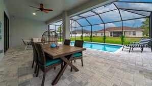 A covered patio with a pool, outdoor furniture, and a view of a house in the background.