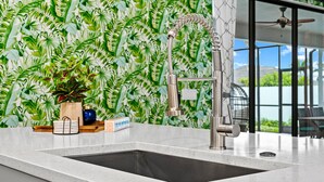 A kitchen with a modern faucet, a sink, and a backsplash with a leafy pattern.