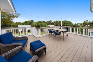 Eine Holzterrasse mit Korbmöbeln und einem Tisch, umgeben von einem weißen Geländer.