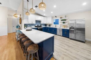 A modern kitchen with a central island, bar stools, a stainless steel refrigerator, and blue cabinets.