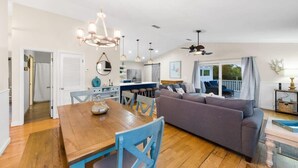 A spacious living area with a wooden dining table, blue chairs, a grey sofa, and a kitchen in the background. - Bid-A-Wee Beach Home-Private Pool (Panama City Beach)