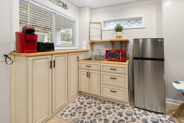 A compact kitchen with a stainless steel refrigerator, a microwave, and a coffee maker on the counter.