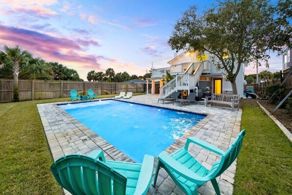 A backyard with a swimming pool, a wooden deck, and a house with a porch.