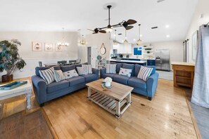 Una sala moderna con un sofá azul, una mesa de centro de madera y una cocina al fondo.