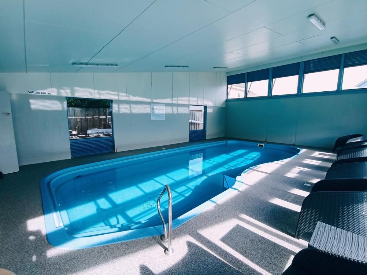 Una piscina interior con agua cristalina, un trampolín y una zona soleada con asientos.