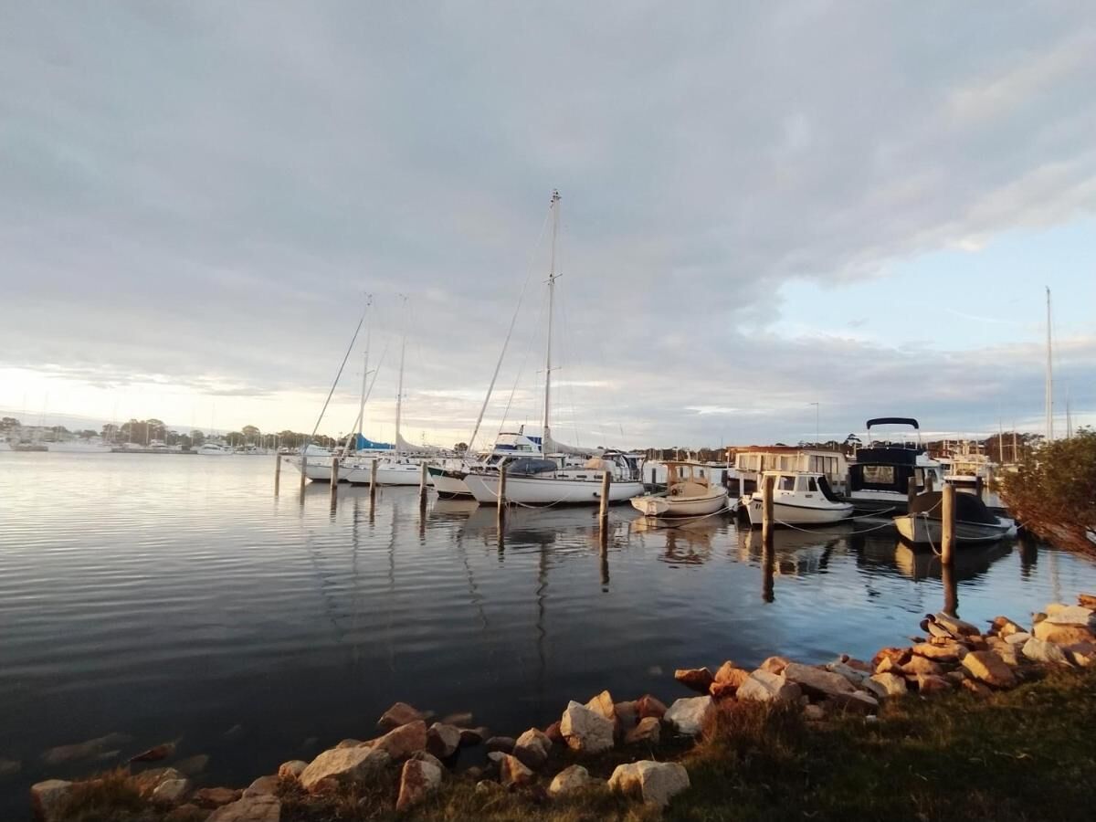 A marina with several boats docked, calm water, and a rocky shoreline.