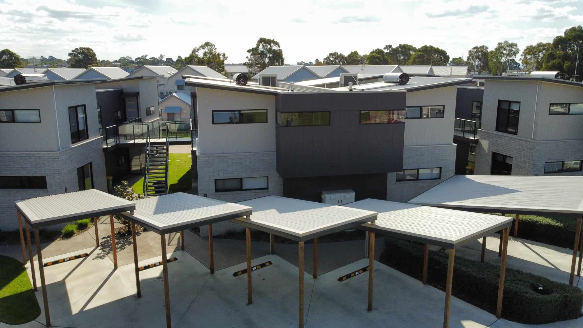 A modern multi-story residential building with a flat roof, large windows, and a covered outdoor area with tables.