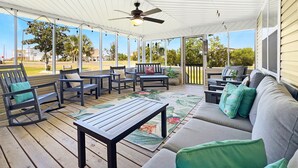 Eine überdachte Terrasse mit Holzboden, einem Deckenventilator und Gartenmöbeln, darunter Stühle, ein Tisch und eine Sitzecke.