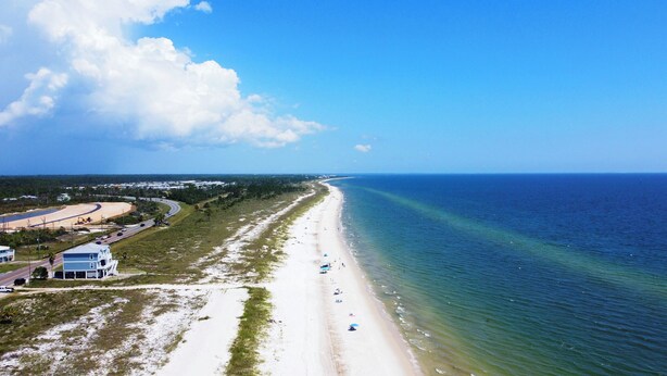 Eine Küstenstraße mit Strand, blauem Himmel und einigen Gebäuden.