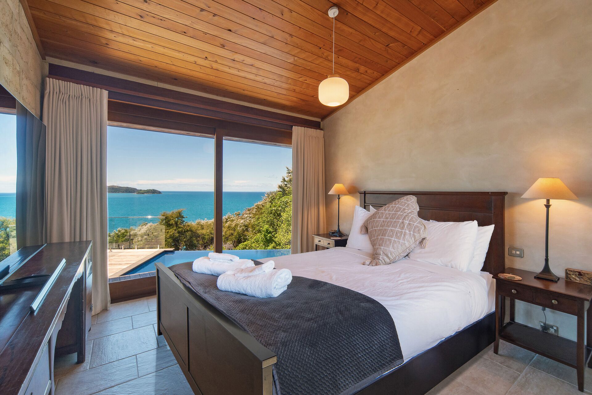 Une chambre avec un grand lit, deux lampes de chevet, un piano et une vue sur la mer.