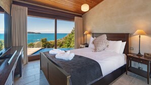 Een slaapkamer met een groot bed, twee bedlampen, een piano en uitzicht op zee.