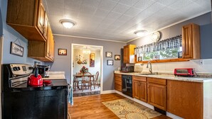 Una cocina con armarios de madera, un hervidor rojo, un microondas y una zona de comedor con una mesa y sillas.