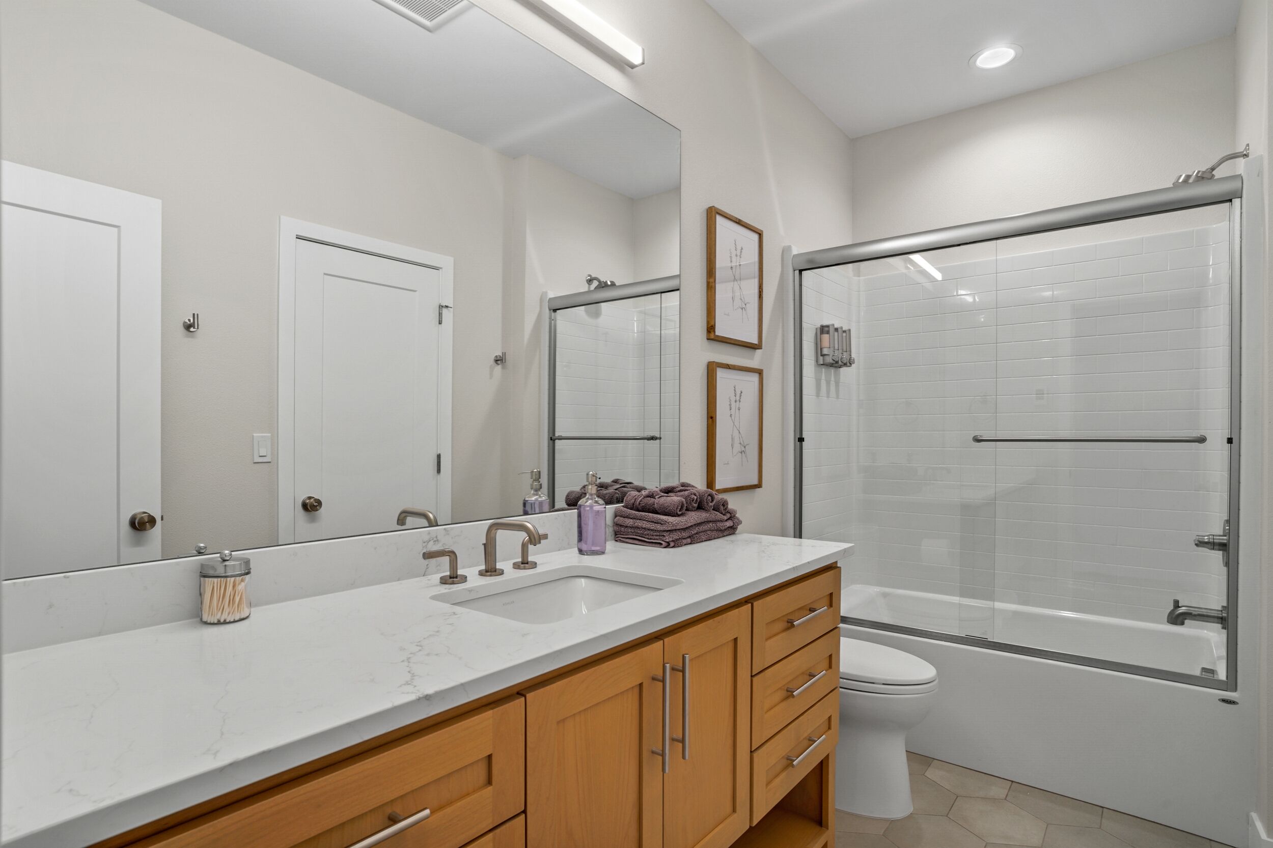Un baño moderno con un espejo grande, un lavabo, un inodoro y una ducha con mampara de vidrio.