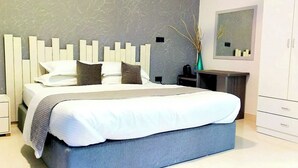 A modern bedroom with a large bed, a bedside table, a nightstand, a wardrobe, and a mirror on the wall. - Turtle Inn Dharavandhoo (Dharavandhoo)