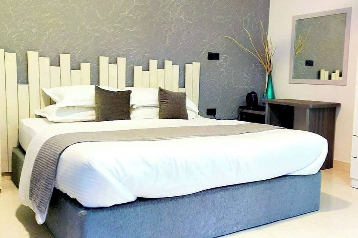 A modern bedroom with a large bed, a bedside table, a nightstand, a wardrobe, and a mirror on the wall.