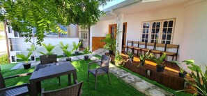 Un patio con una mesa y sillas, rodeado de plantas en macetas y una pequeña zona de césped.