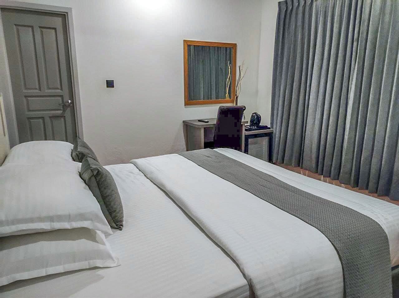 A hotel room with a bed, a desk, a chair, a window with curtains, and a door.