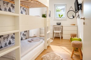 A child's bunk bed with a forest-themed wall, a desk with a chair, and a small stool.