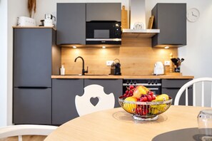 A modern kitchen with grey cabinets, a microwave, and a fruit bowl on the table.