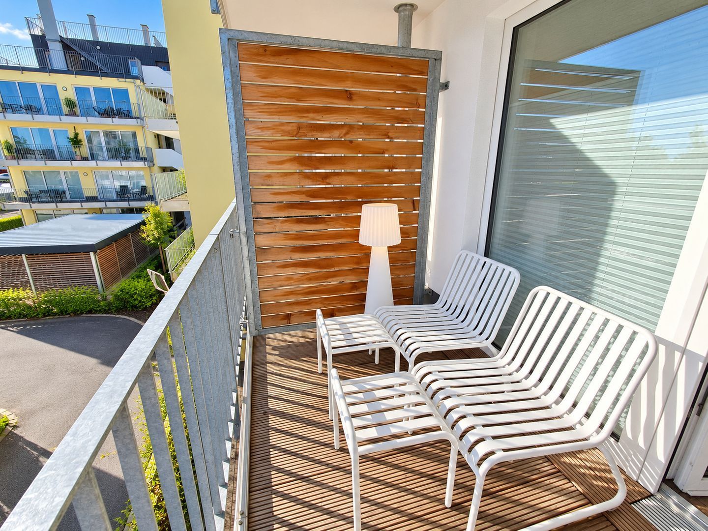 Un balcon avec des chaises en métal blanc et une cloison en lattes de bois.