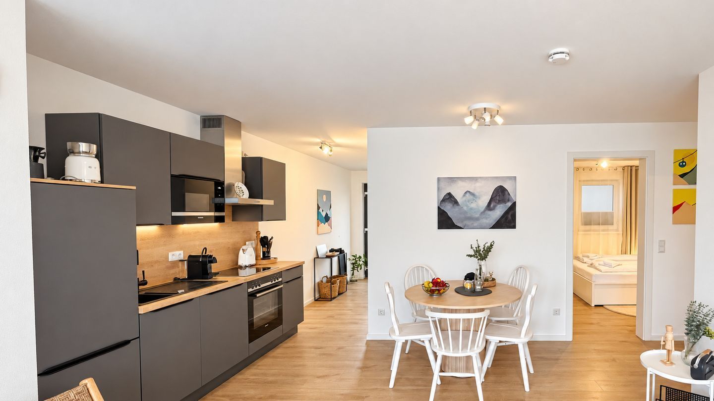 A modern kitchen with dark cabinetry, a wooden countertop, and a dining area with white chairs.