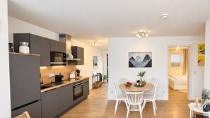 Una cocina moderna con armarios oscuros, una encimera de madera y una zona de comedor con sillas blancas.