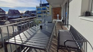 Un balcón con una mesa para dos, una banca y vistas de la ciudad.