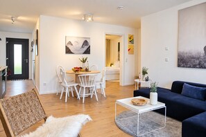 Un salon moderne avec un canapé bleu foncé, une table de salle à manger ronde entourée de chaises blanches et une table basse blanche.