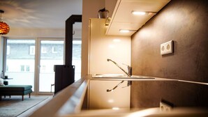 A modern kitchen with a glass countertop, stainless steel sink, and a view of the outside through large windows. - Moderne Ferienwohnung im Stadtzentrum: 3 Zimmer, Südbalkon und Infrarotkabine für Max. 4 Personen - (Winterberg)