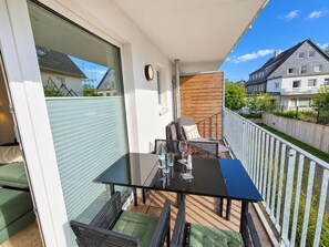Een balkon met een glazen tafel, stoelen en een houten hek.