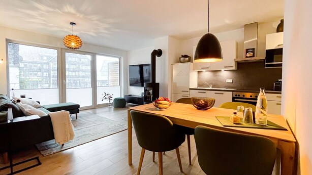 A modern apartment with a dining area, kitchen, and a living room with a sofa and a TV. - Moderne Ferienwohnung im Stadtzentrum: 3 Zimmer, Südbalkon und Infrarotkabine für Max. 4 Personen - (Winterberg)
