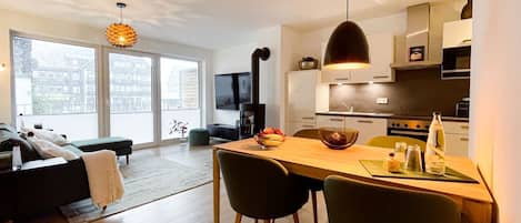 A modern apartment with a dining area, kitchen, and a living room with a sofa and a TV.