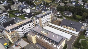 A modern multi-story building with a mix of residential and commercial spaces, featuring a central courtyard and a parking area. - Moderne Ferienwohnung im Stadtzentrum: 3 Zimmer, Südbalkon und Infrarotkabine für Max. 4 Personen - (Winterberg)