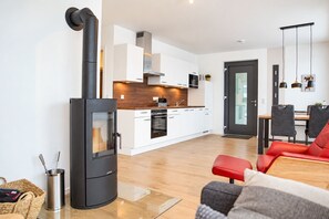 A modern kitchen with white cabinets, a built-in oven, and a black stove. There is a dining area with a red sofa and a table.