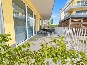 A balcony with a table and chairs, a glass door, and a white fence.