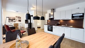 A modern kitchen with white cabinets, a microwave, and a stove. There is a dining area with a wooden table and chairs. - Moderne Ferienwohnung für 4 Personen in Bester Stadtlage - Gebirgsresort (Winterberg)