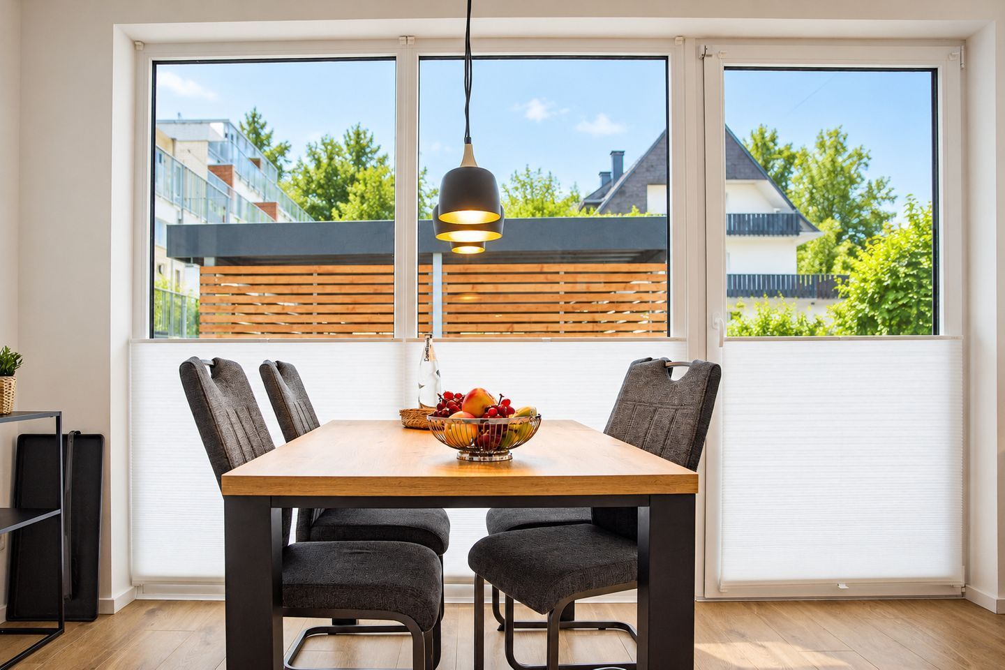 Un coin repas avec une table en bois, quatre chaises, un saladier rempli de fruits et une suspension.