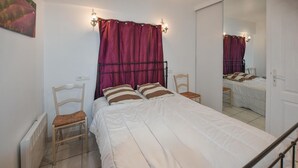 Un dormitorio con una cama, dos sillas, un radiador y un espejo.