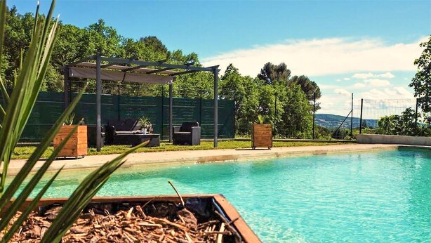 Piscina con pérgola y zona de estar, rodeada de vegetación.