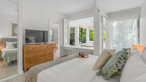 Un dormitorio moderno con una cama grande, un aparador de madera, un televisor de pantalla plana y vistas a la vegetación a través de amplias ventanas.