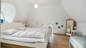 Une chambre avec un plafond en pente, un lit avec une literie blanche, une table de chevet avec une lampe, un miroir et des éléments de décoration murale.