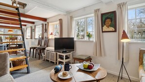 Un salon confortable avec un téléviseur, un coin repas et un tableau accroché au mur.