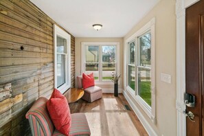 A cozy room with a wooden wall, a cushioned bench, a small table, and large windows offering a view of the outdoors. - Home w/ porch in DT Libertyville Near Naval Base (Libertyville)