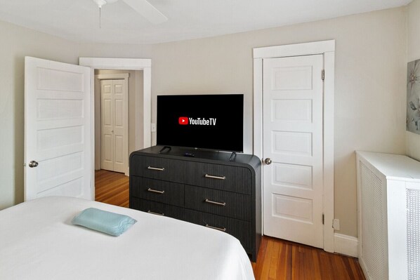 A hotel room with a bed, a TV on a dresser, and two doors.