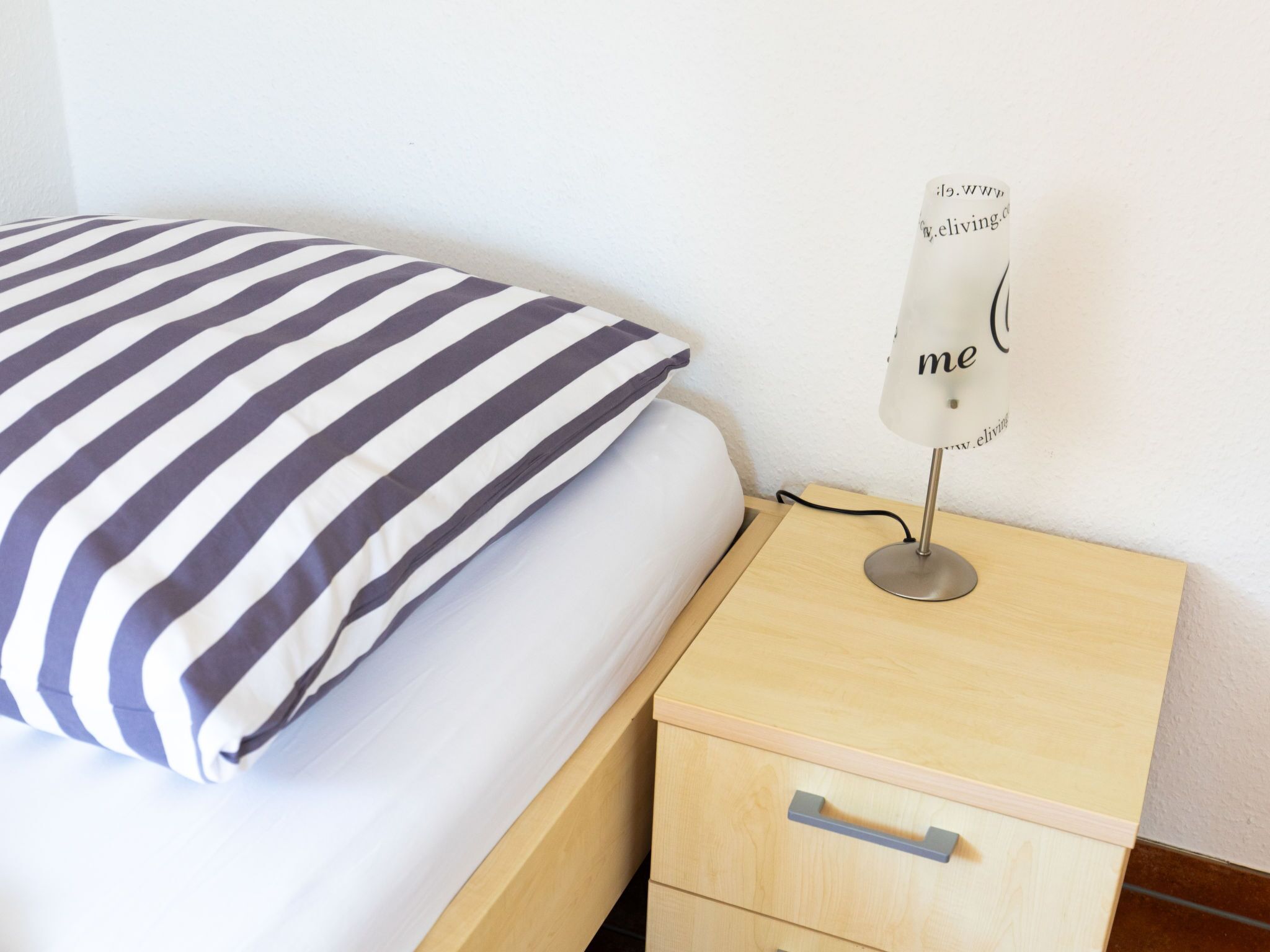 A bed with a striped pillow, a bedside table with a lamp, and a drawer.