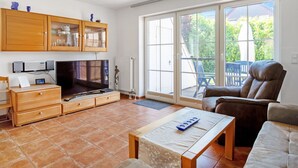 A spacious living room with a TV, wooden cabinets, and a sliding glass door leading to an outdoor area. - Haus 99 - Seepark Burhave by Interhome (Burhave)