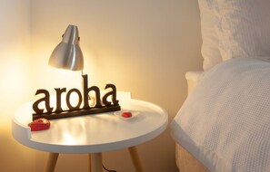 A bedside table with a lamp, a decorative sign spelling "aroba," and a small red object on it. - The Love Shack (Arthur's Point)