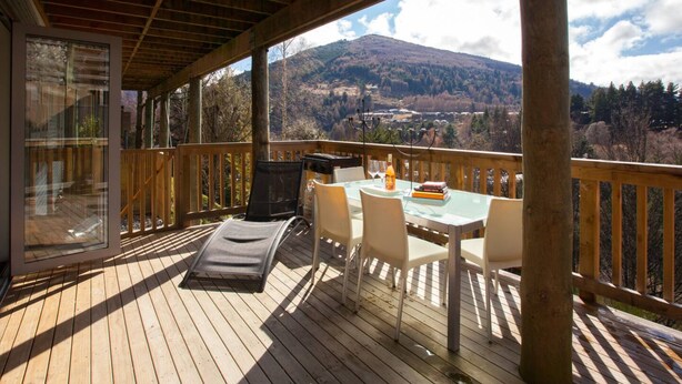 Una terrazza in legno con tavolo e sedie, un barbecue e una porta vetrata che dà su una stanza.