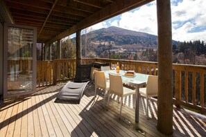 Eine Holzterrasse mit Tisch, Stühlen, einem Grill und einer Glastür zu einem Raum.